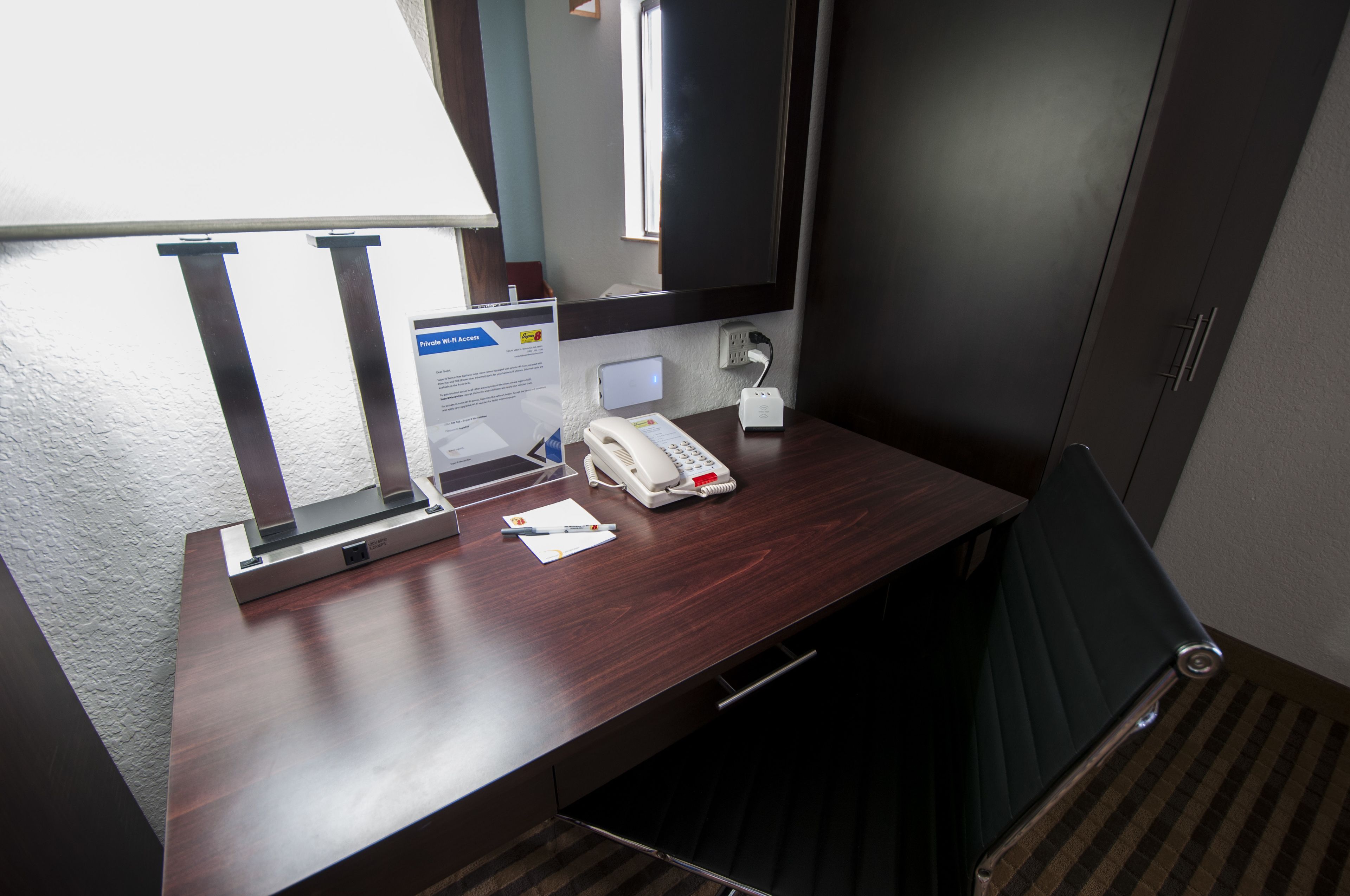 Une chambre d’hôtel avec un bureau en bois, un téléphone, une prise électrique et une fenêtre.