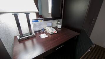 Une chambre d’hôtel avec un bureau en bois, un téléphone, une prise électrique et une fenêtre.