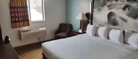 Habitación de hotel con una cama grande, un escritorio, una silla, una lámpara y un cuadro de una cascada.