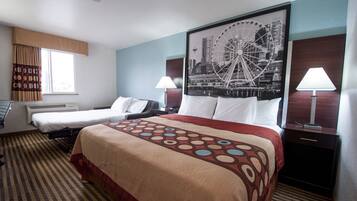A hotel room with a large bed, two smaller beds, a desk, a chair, a lamp, and a wall-mounted TV.