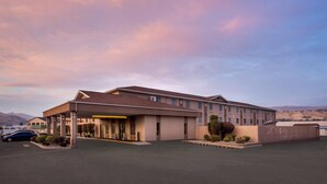 A hotel with a covered entrance, a parking lot, and a mountainous backdrop.