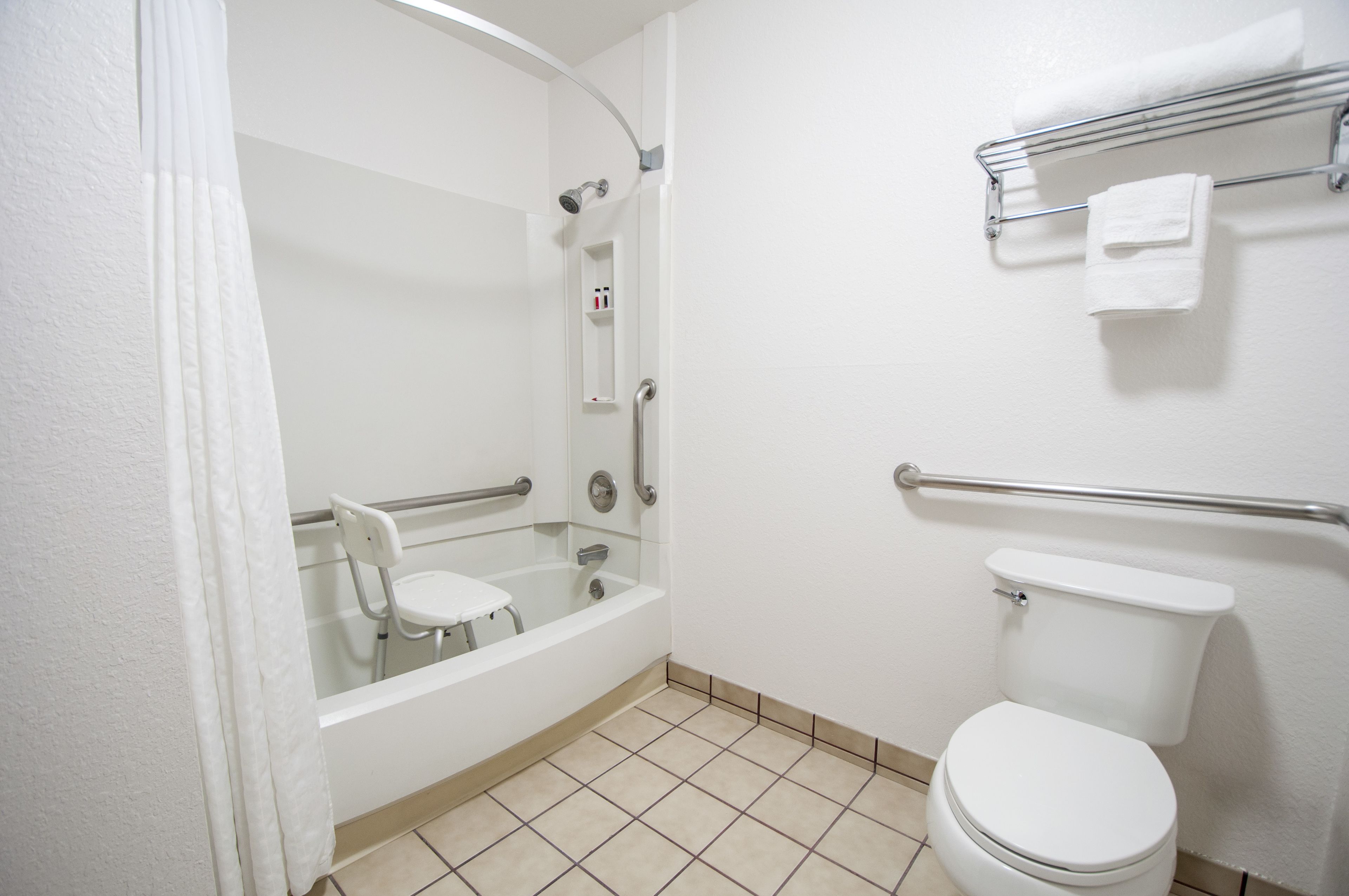 A bathroom with a bathtub, toilet, and a handrail.
