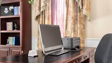 A laptop on a desk with a printer, a bookshelf with books and a trophy, and a window with curtains.