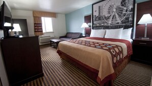 A hotel room with a large bed, a desk, a chair, a TV, and a window with curtains.