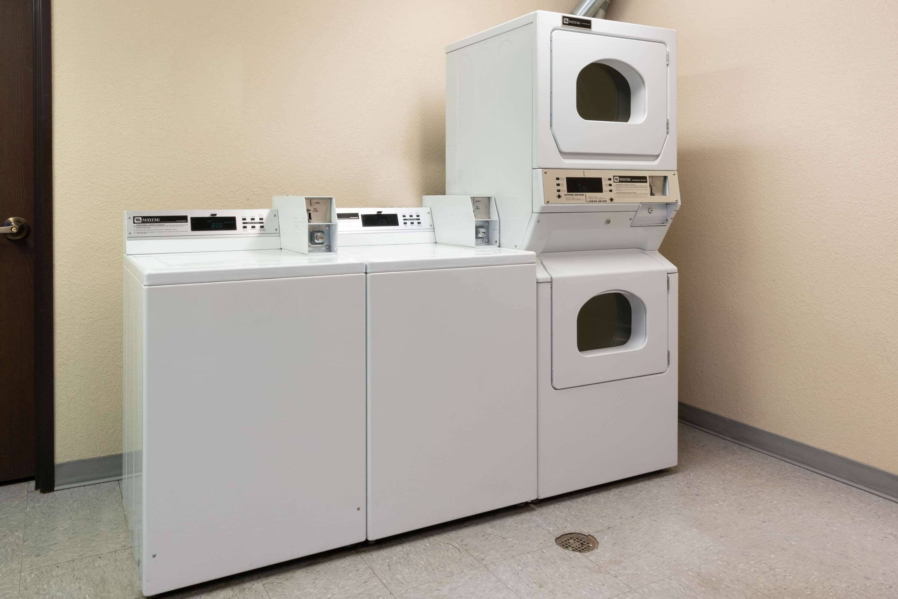 A laundry room with two stacked washers and dryers, a control panel, and a door.