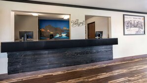 Un mostrador de recepción con detalles de madera oscura, un letrero de bienvenida, un monitor de computadora y un cartel enmarcado con el saludo de Spokane Valley.
