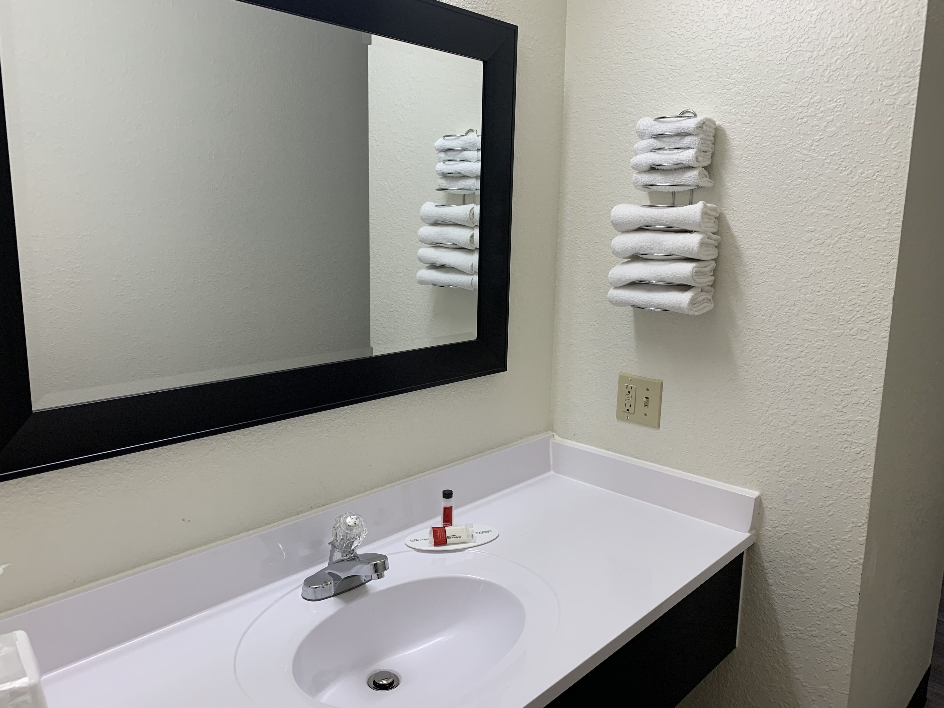 A bathroom with a white sink, a mirror, and a towel rack with folded towels.