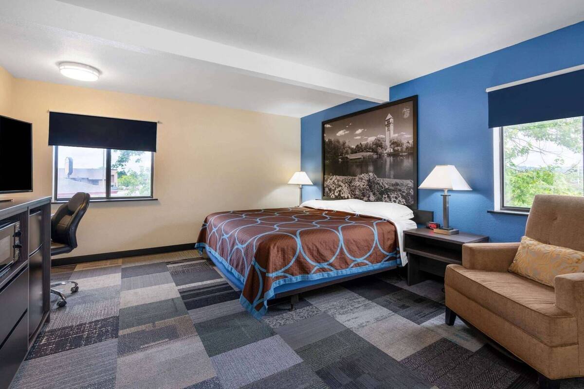 A hotel room with a bed, desk, chair, and a large window.