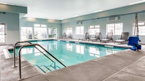 Una piscina interior con agua cristalina azul, una escalera metálica y varias sillas de descanso alrededor de la zona de la piscina.