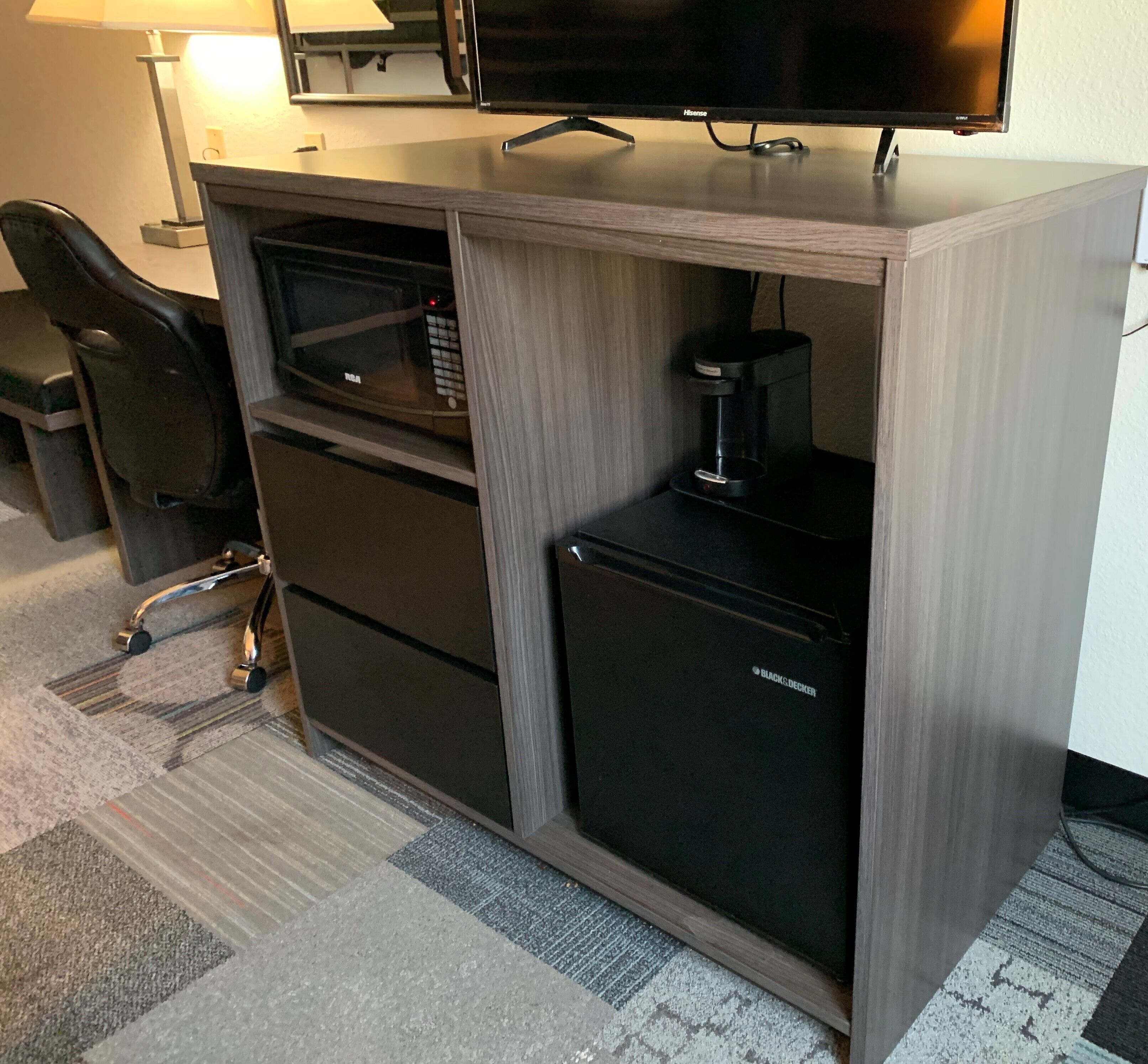A compact office space with a desk, chair, and a small black refrigerator.