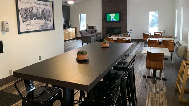 A modern dining area with a long table, chairs, and a television mounted on the wall. - Super 8 by Wyndham Spokane Valley (Spokane Valley)