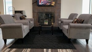 Una sala de estar con una televisión de pantalla plana montada en una pared de piedra, dos sillones grises, una mesita y una chimenea.