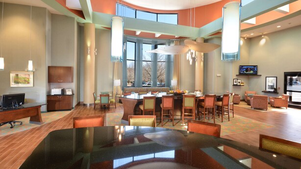 A spacious lobby with a large glass table, comfortable seating, a reception desk, and a television.