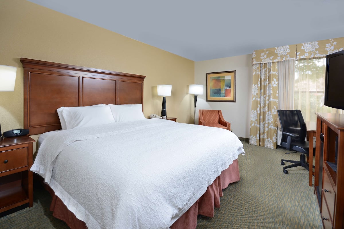 A hotel room with a large bed, two bedside tables, a desk with a chair, a television, and a window with curtains.