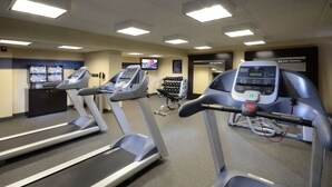 A gym with treadmills, a weight bench, and a television screen displaying an exercise video.