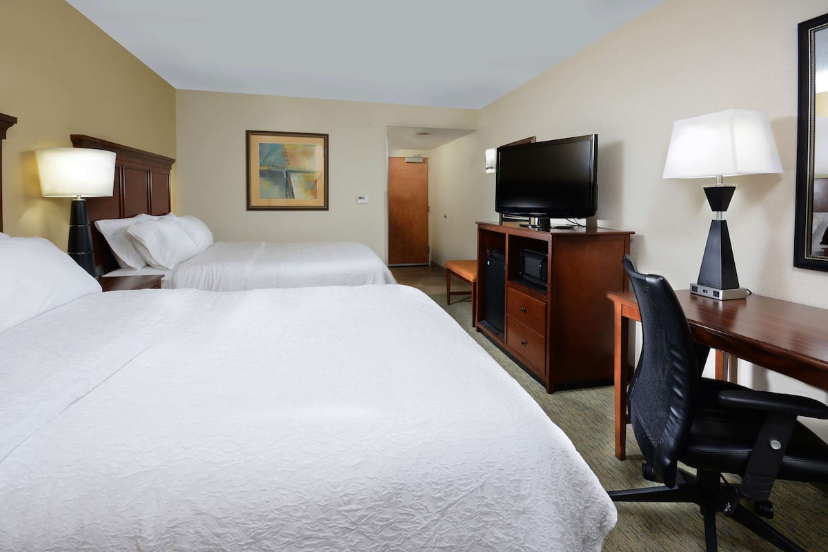 A hotel room with two beds, a desk with a television, a chair, and a lamp.