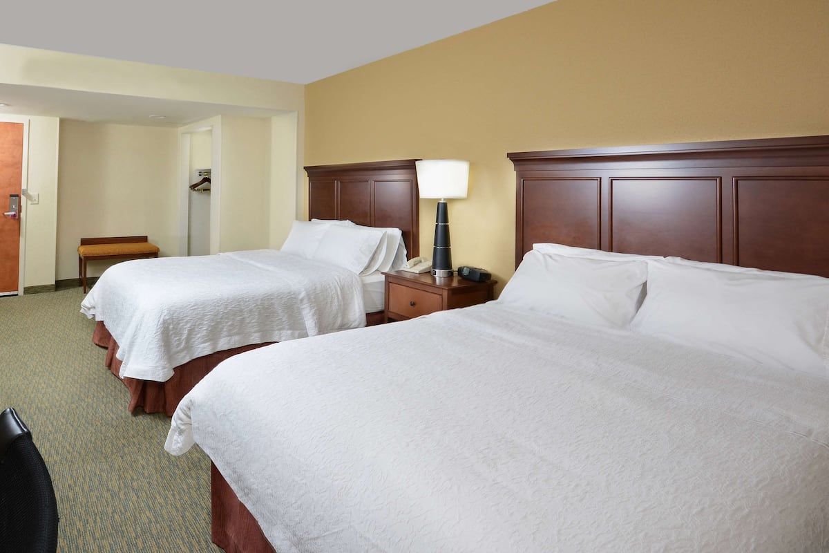 A hotel room with two beds, a bedside table with a lamp, a telephone, and a coat stand.