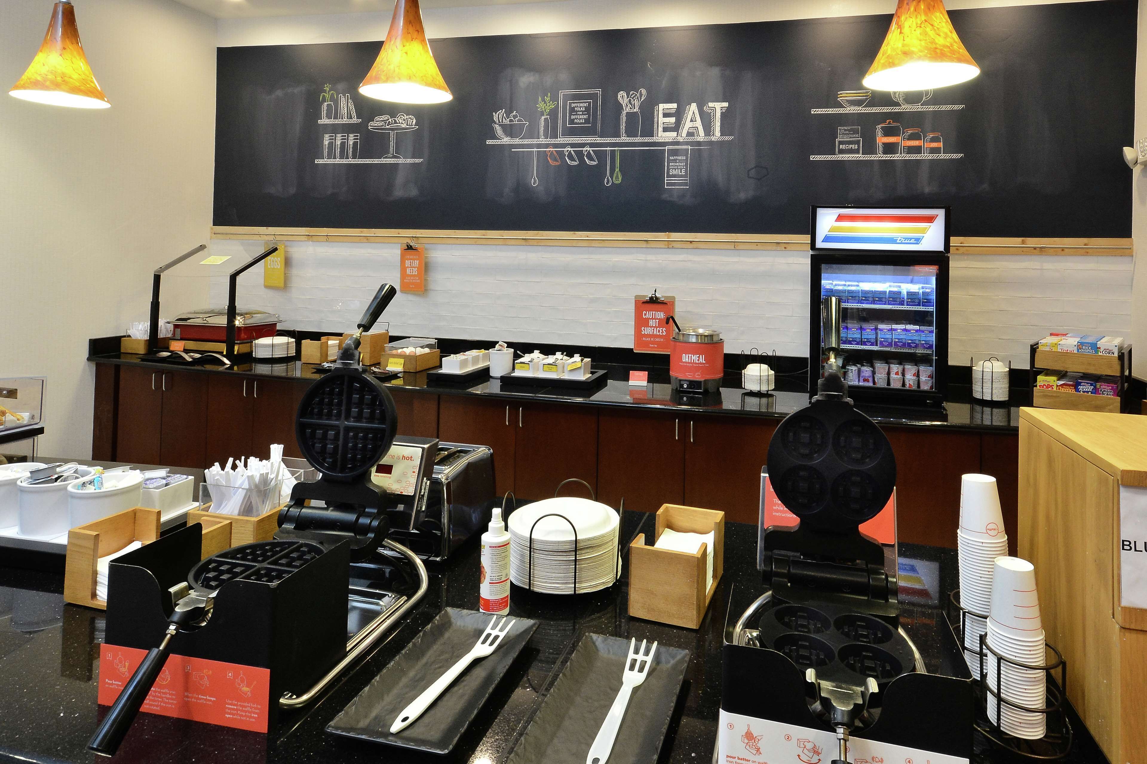 A breakfast bar with waffle makers, a coffee machine, and a beverage dispenser.
