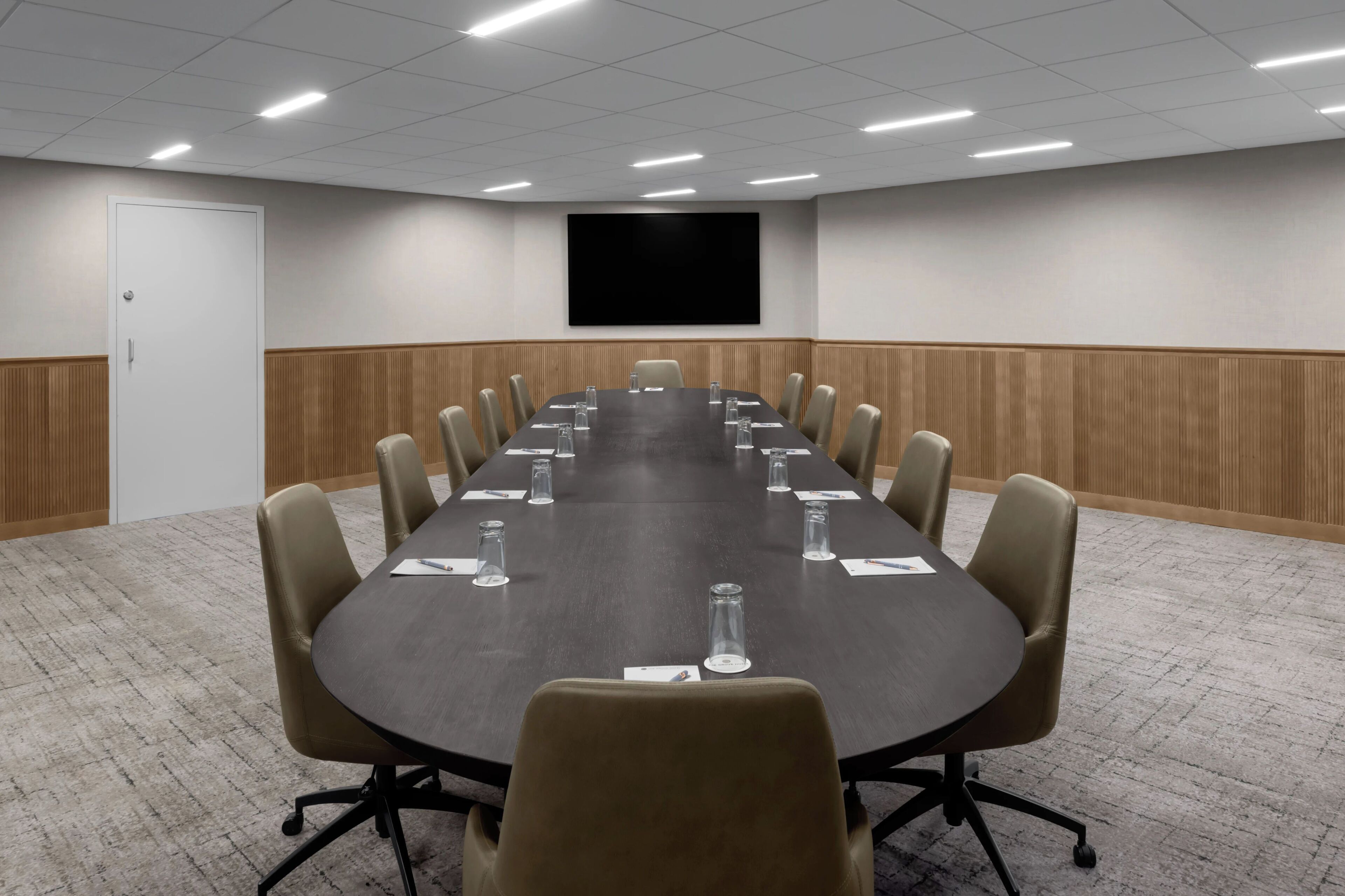 A conference room with a long table, chairs, a screen, and a door.