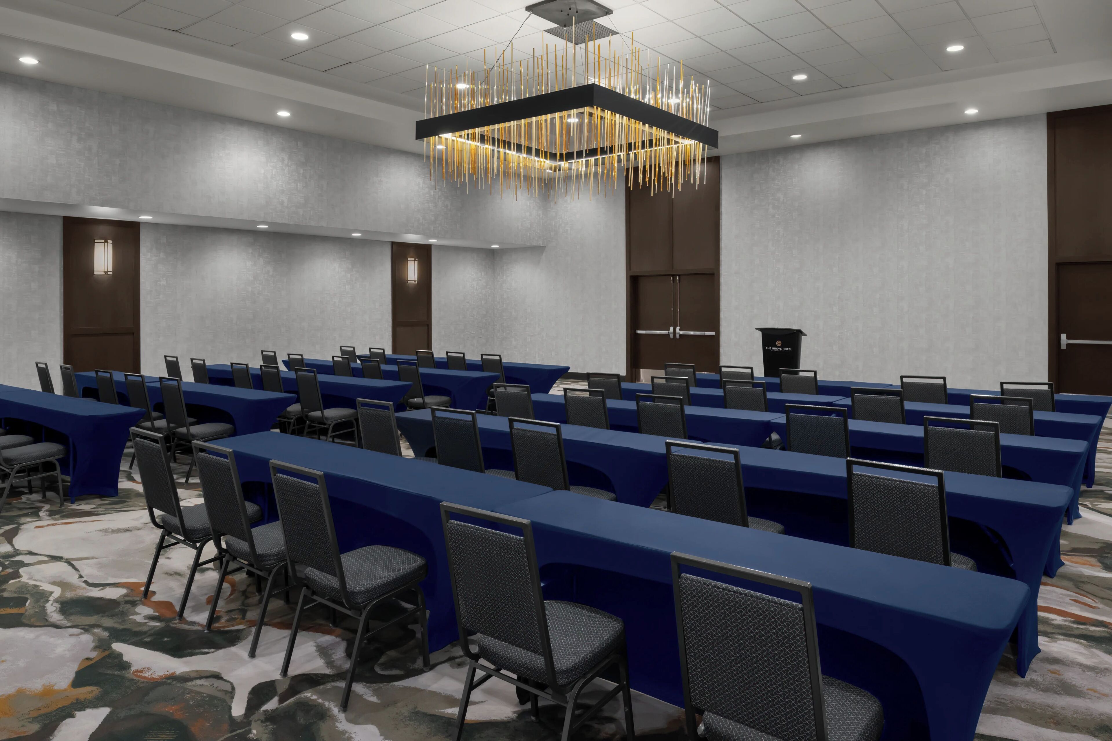 A conference room with long tables, chairs, a podium, and a modern chandelier.