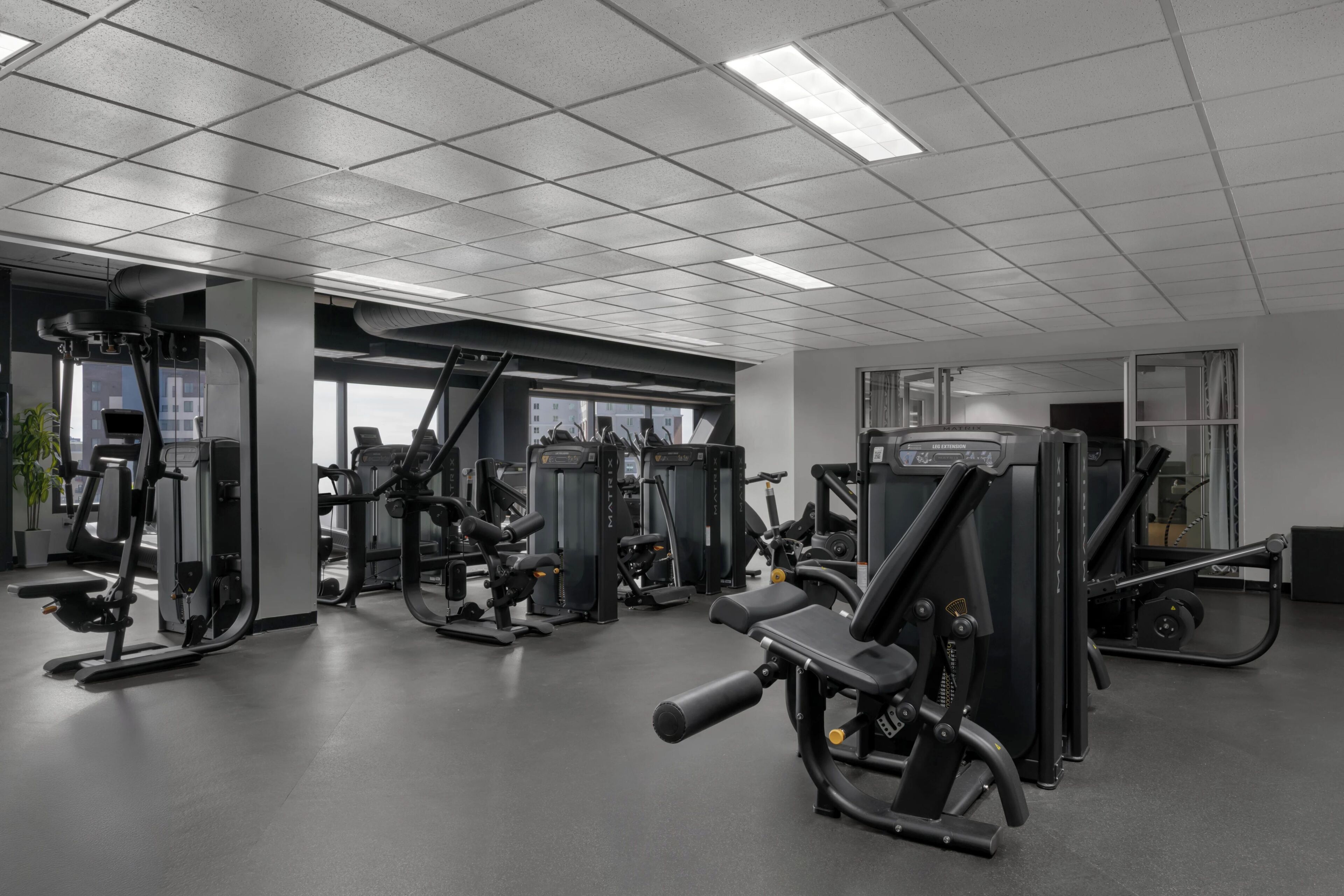 A gym with various exercise machines, a large window, and a ceiling with fluorescent lights.