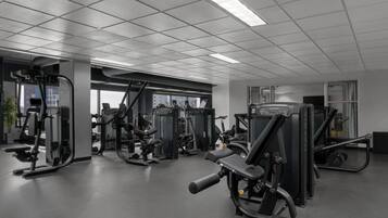 A gym with various exercise machines, a large window, and a ceiling with fluorescent lights.