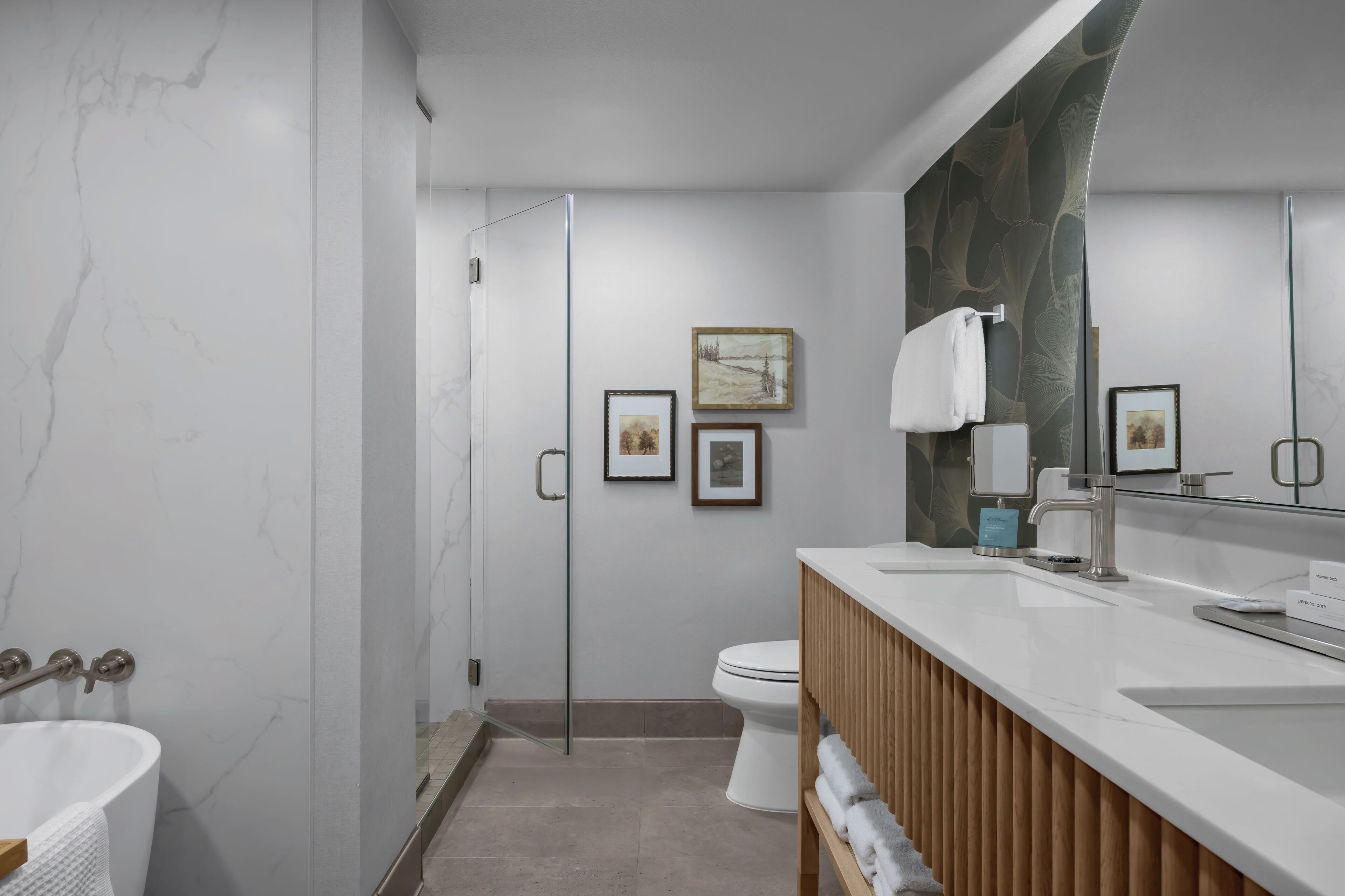 A modern bathroom with a marble wall, a glass shower enclosure, a toilet, and a vanity with a mirror.