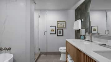 A modern bathroom with a marble wall, a glass shower enclosure, a toilet, and a vanity with a mirror.