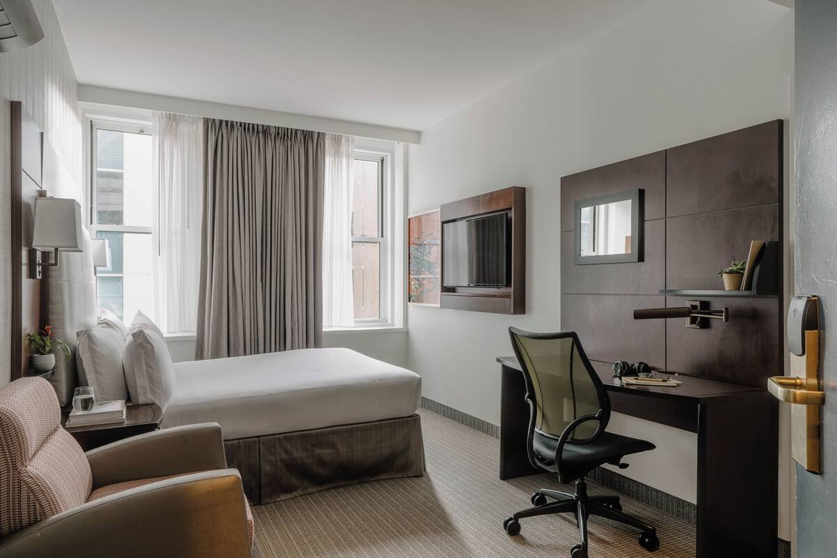 Een hotelkamer met een bed, een bureau, een stoel, een televisie en een raam met gordijnen.
