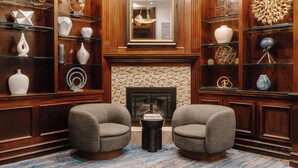 A modern lobby with a fireplace, two armchairs, and a variety of decorative items on shelves. - Club Quarters Hotel Faneuil Hall, Boston (Boston)