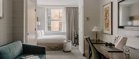 Une chambre d’hôtel avec un lit, un bureau avec un ordinateur portable, une chaise, une valise et un canapé.