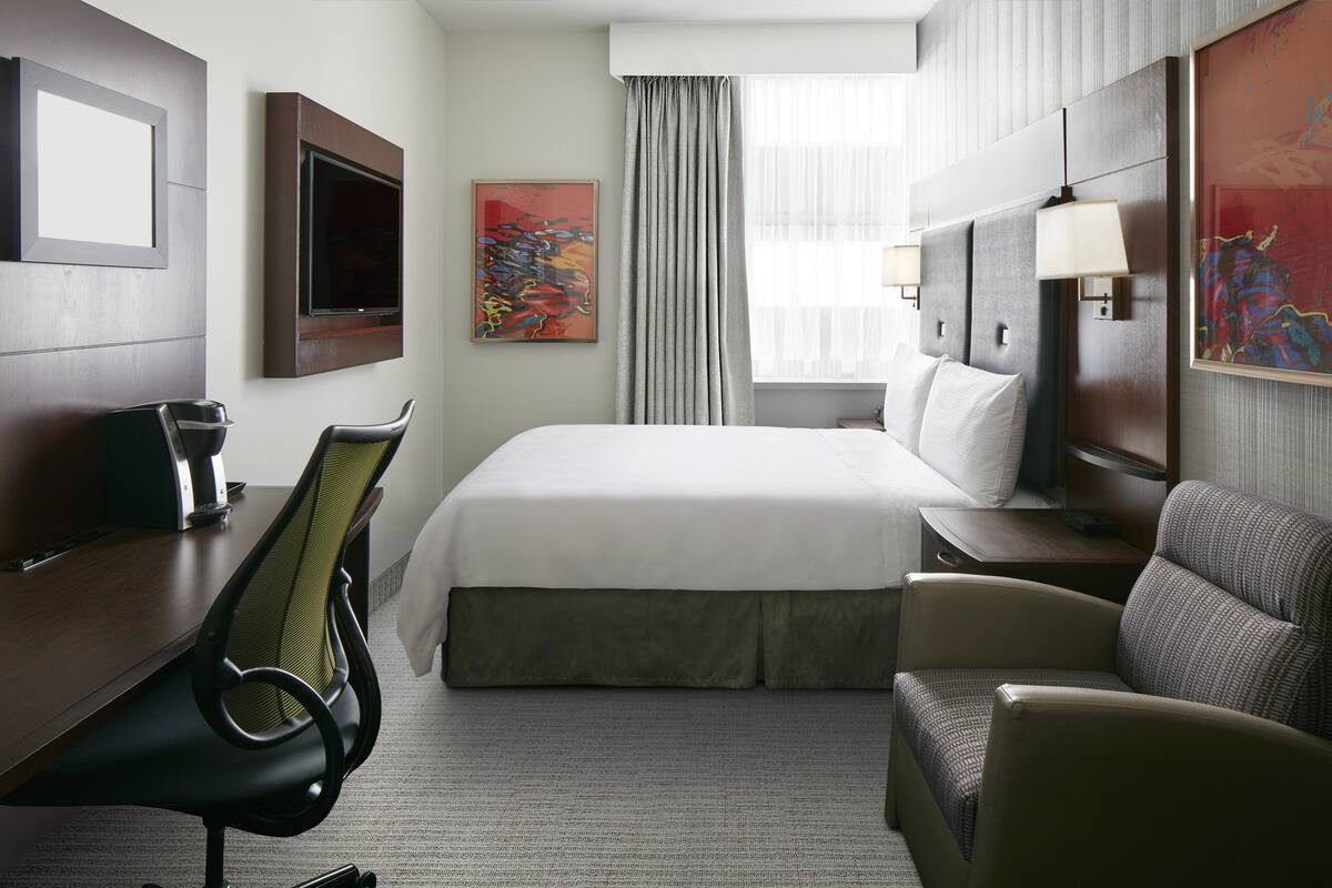 Een hotelkamer met een bed, een bureau, een stoel, een lamp en kunst aan de muren.