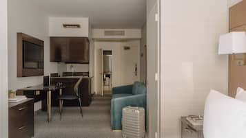 A hotel room with a bed, a desk, a chair, a sofa, a suitcase, and a TV.