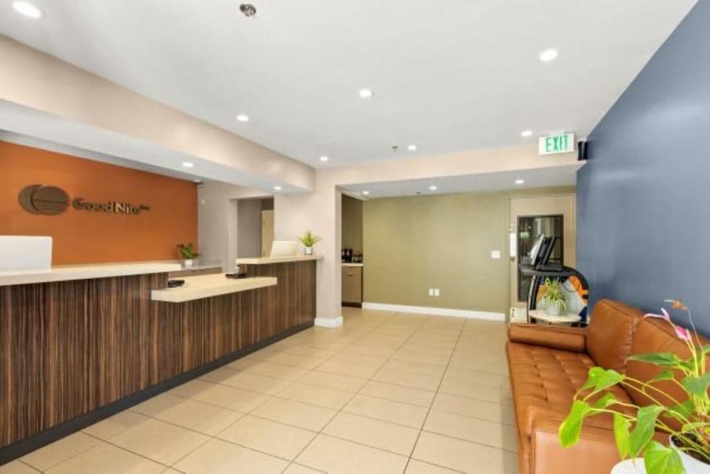 Un área de recepción con un mostrador de madera, una zona de estar con un sofá de cuero marrón y una señal de salida en la pared.
