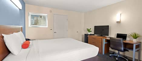 A hotel room with a large bed, a desk with a computer, a television, and a small plant.