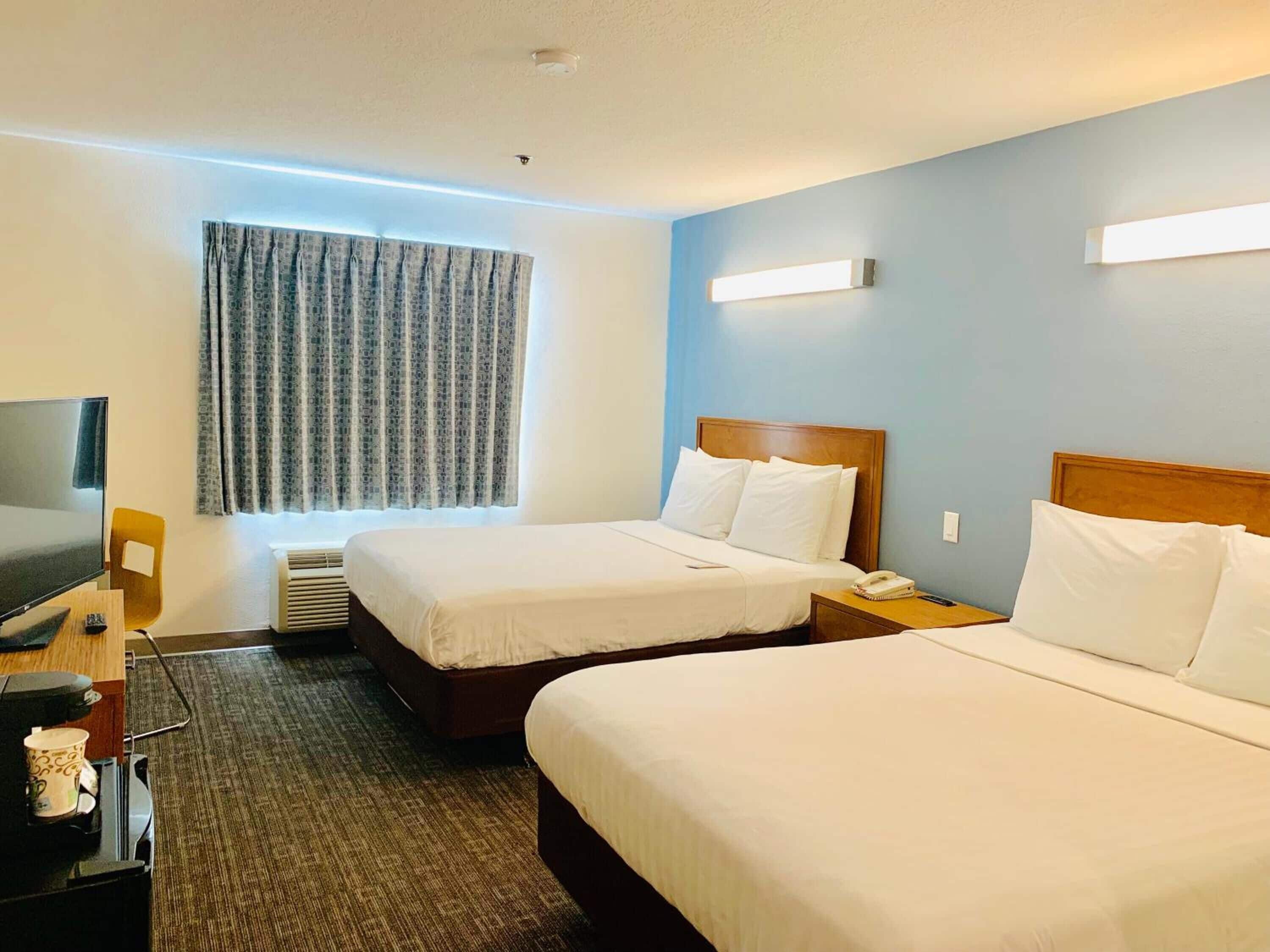 A hotel room with two beds, a desk with a TV, a coffee maker, and a window with curtains.