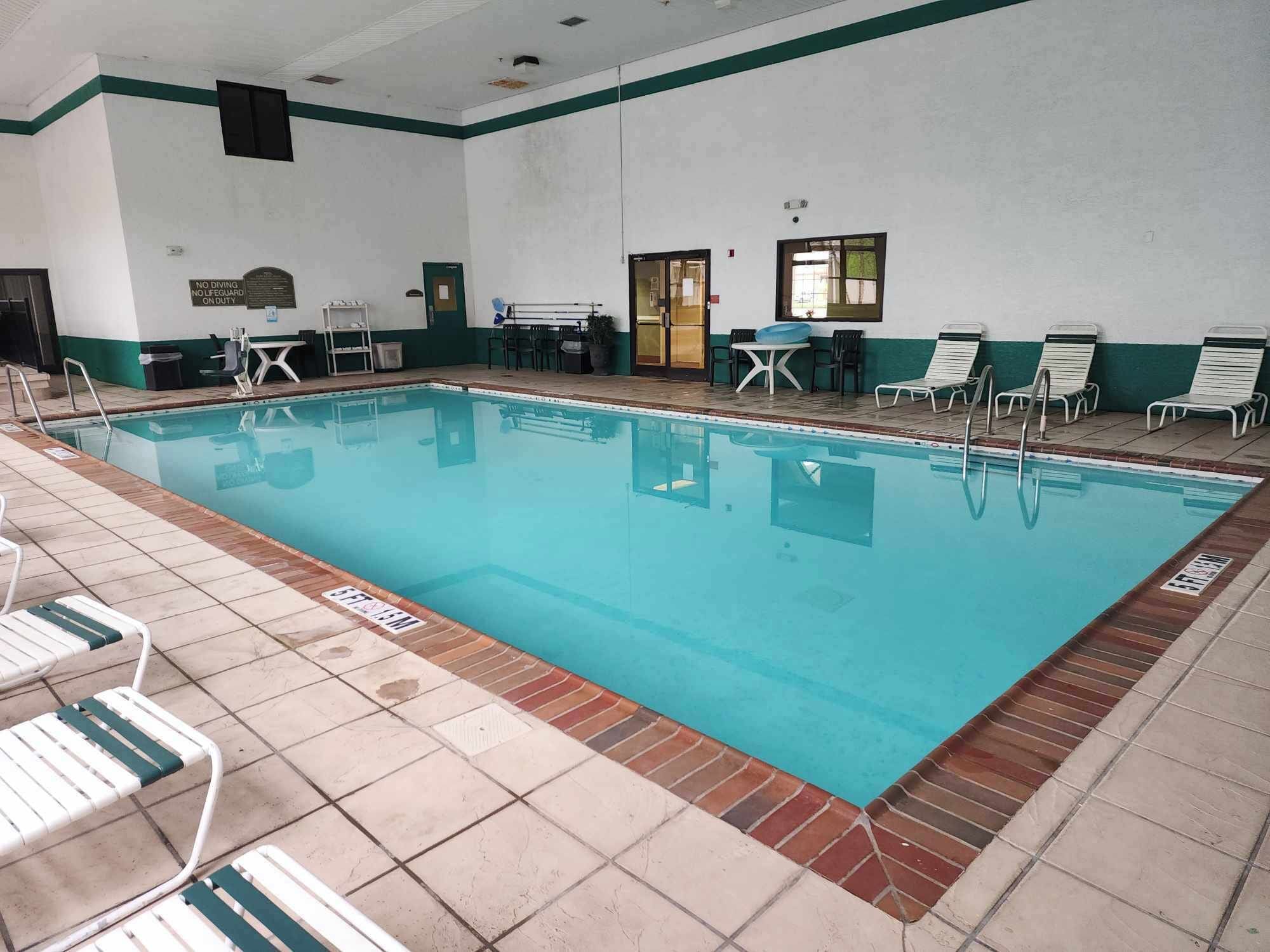 Una piscina con sillas de descanso y una mesa, rodeada de un suelo de baldosas.