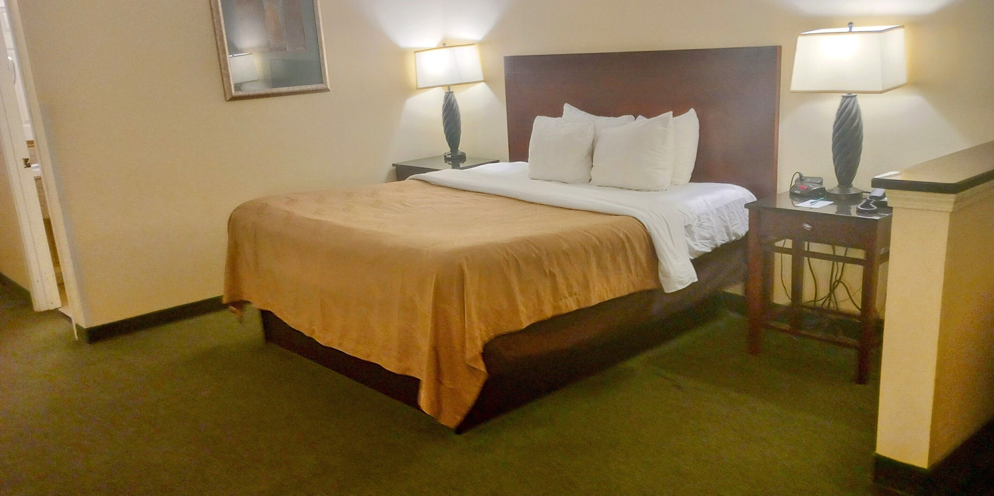 A hotel room with a bed, two bedside lamps, a nightstand, and a framed picture on the wall.