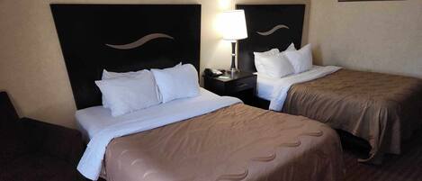 A hotel room with two beds, each with a headboard, a bedside table with a lamp, and a painting on the wall.