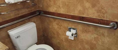 Un baño con inodoro, barra de apoyo y toallero.