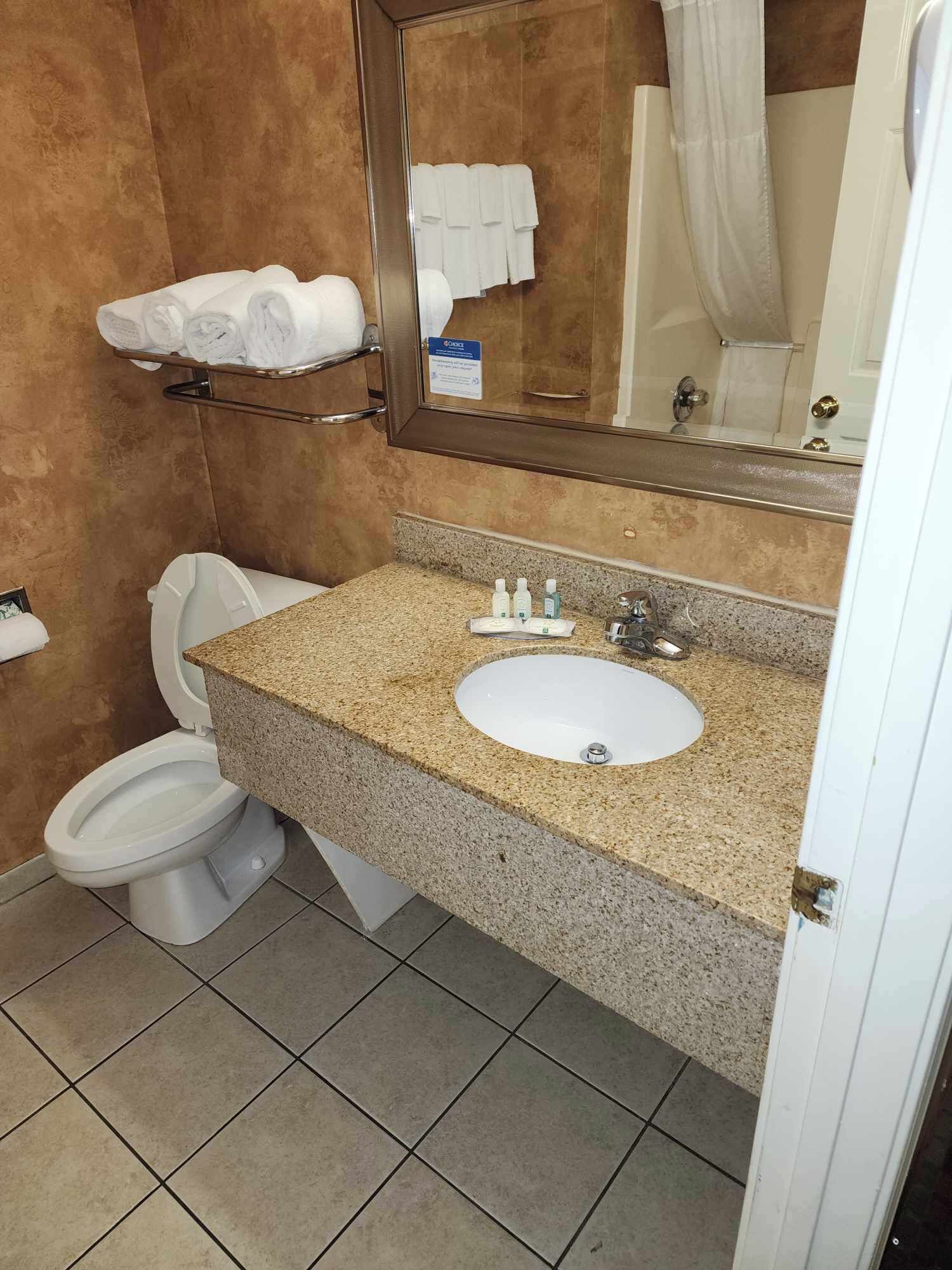 Un baño con inodoro blanco, lavamanos con encimera de granito y un espejo sobre el lavamanos.