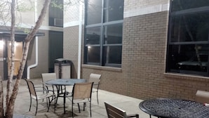 An outdoor patio area with a round table and chairs, a brick wall, and large windows.