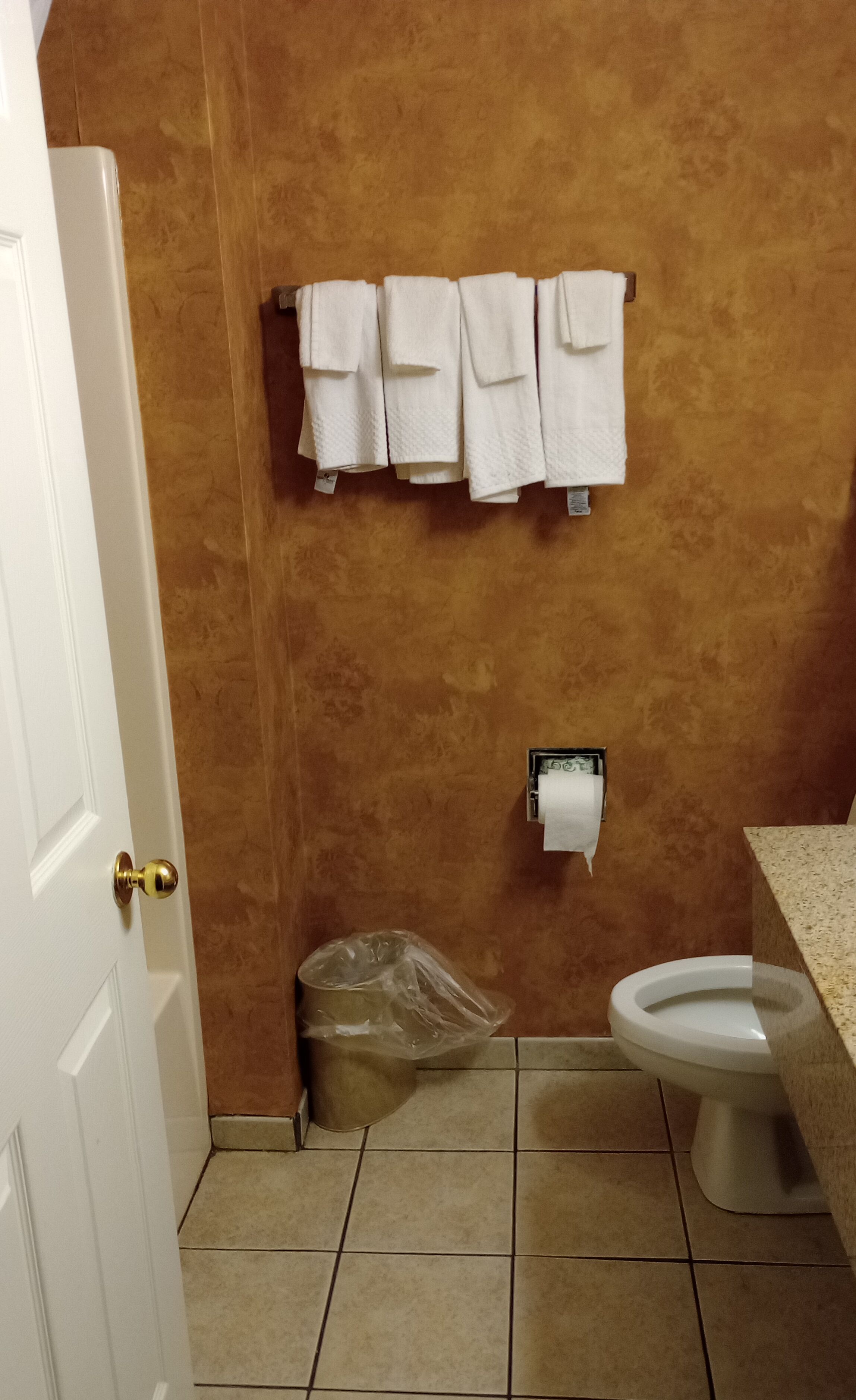A bathroom with a toilet, a trash can, and a towel rack with several towels.
