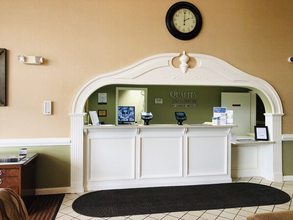 A reception desk with a clock above it, a monitor, and a sign that reads "Quality Inn & Suites by Choice Hotels".