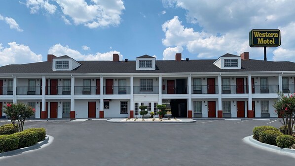 Un motel de estilo occidental con una estructura de dos pisos, entrada central y estacionamiento.