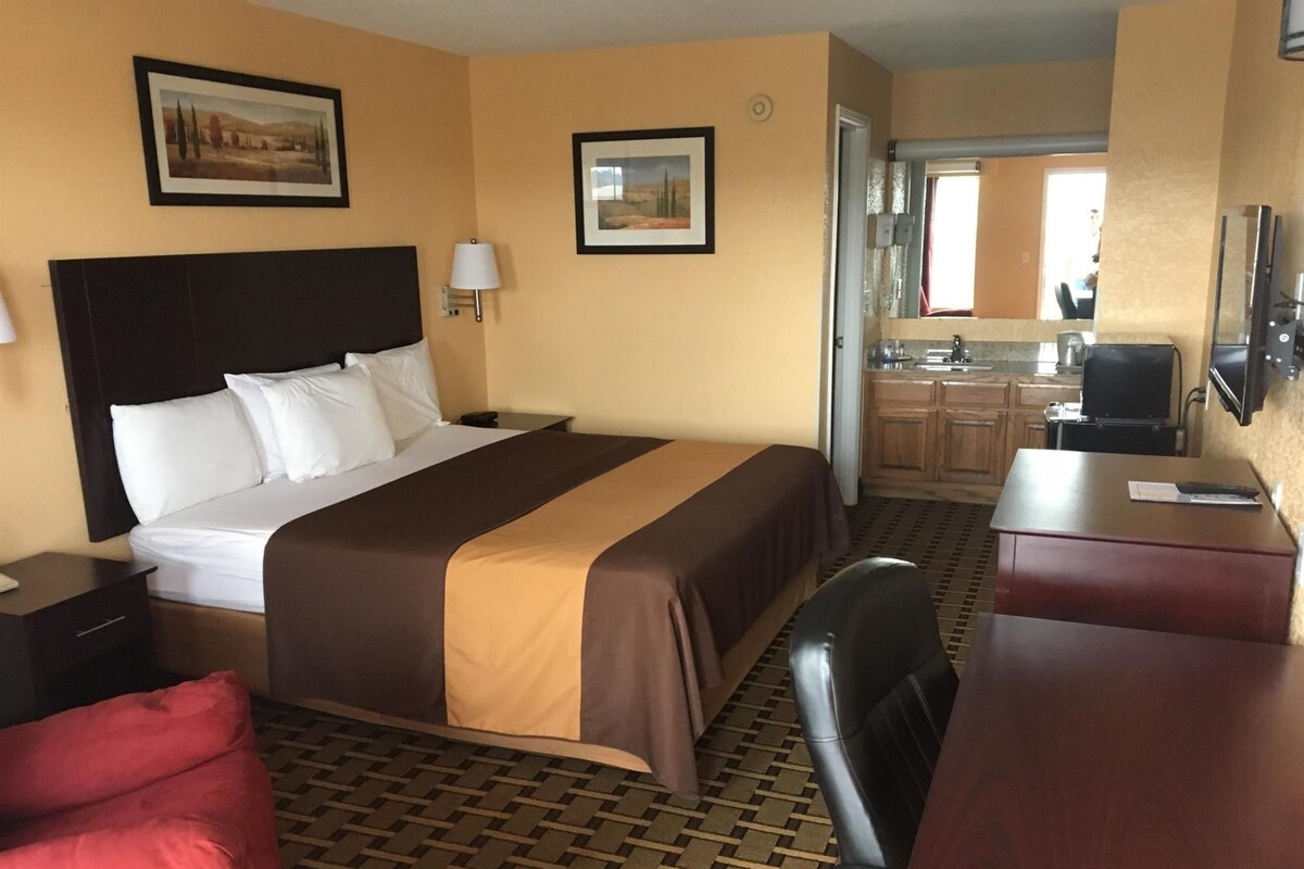 A hotel room with a bed, a desk, a chair, a TV, and a kitchen area.