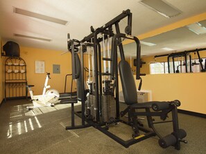 Un gimnasio con equipo de ejercicio, un estante en la pared y una ventana con persianas.