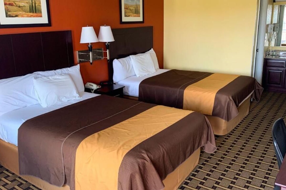 A hotel room with two beds, a nightstand with a lamp, and a bathroom visible through an open door.