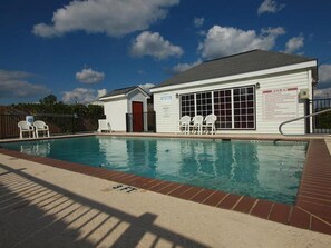 Una piscina con zona cubierta, un pequeño edificio con puerta roja y un cartel que indica las normas.