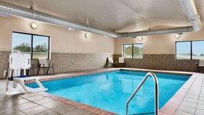 Una piscina interior con agua cristalina, una escalera de piscina y una silla para socorrista.